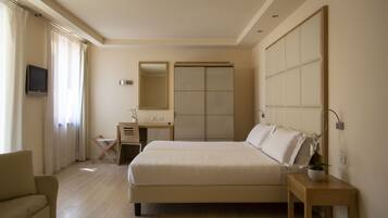 A bedroom with a bed, bedside table, chair, desk, mirror, wardrobe, and a TV.