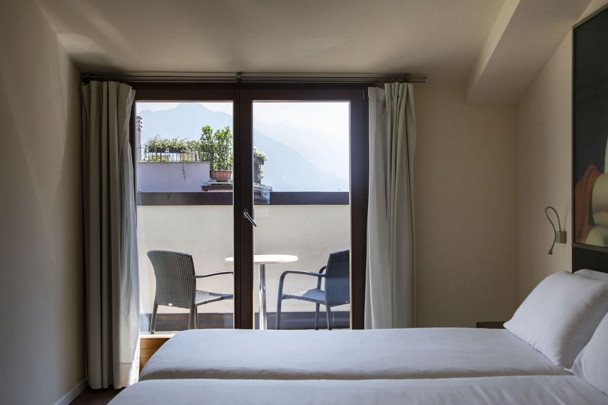 Une chambre d’hôtel avec un lit, un balcon avec deux chaises et une vue sur les montagnes.
