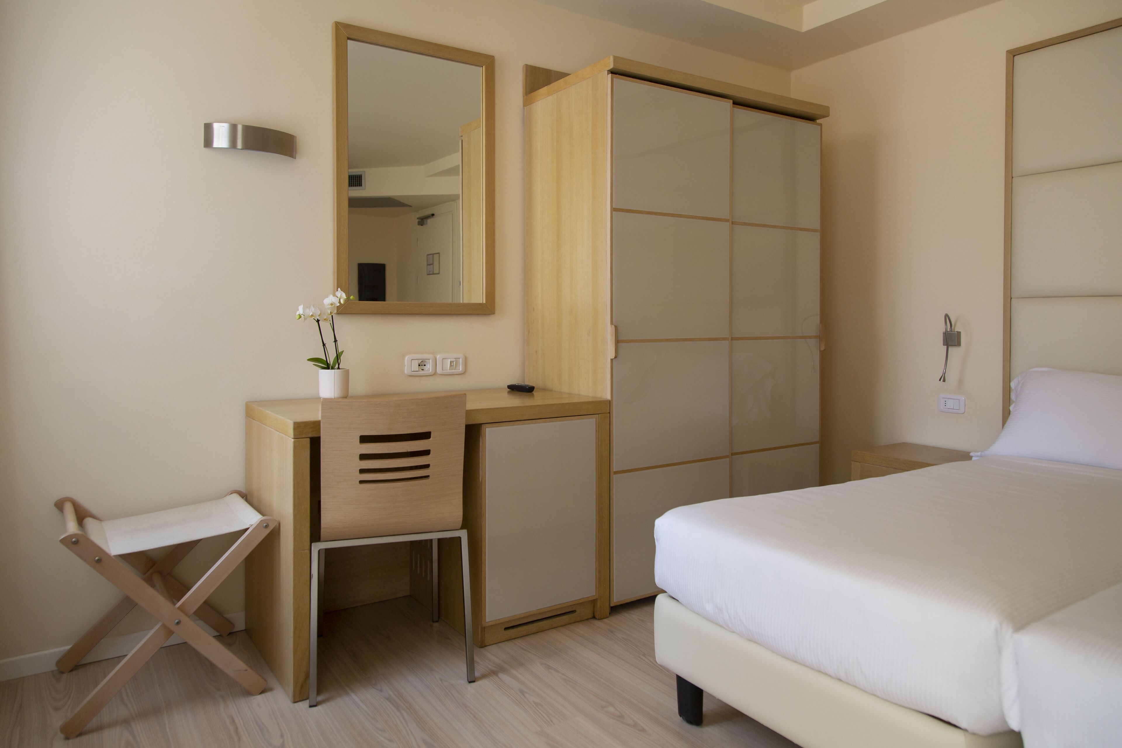 Une chambre d’hôtel de taille réduite, comprenant un lit, un bureau avec une chaise, une armoire et un miroir.