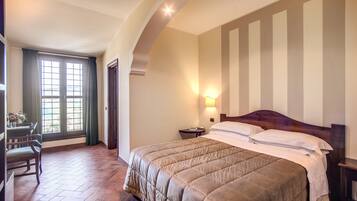 Habitación de hotel con una cama grande, un escritorio con silla, una ventana con cortinas y una lámpara fijada en la pared.