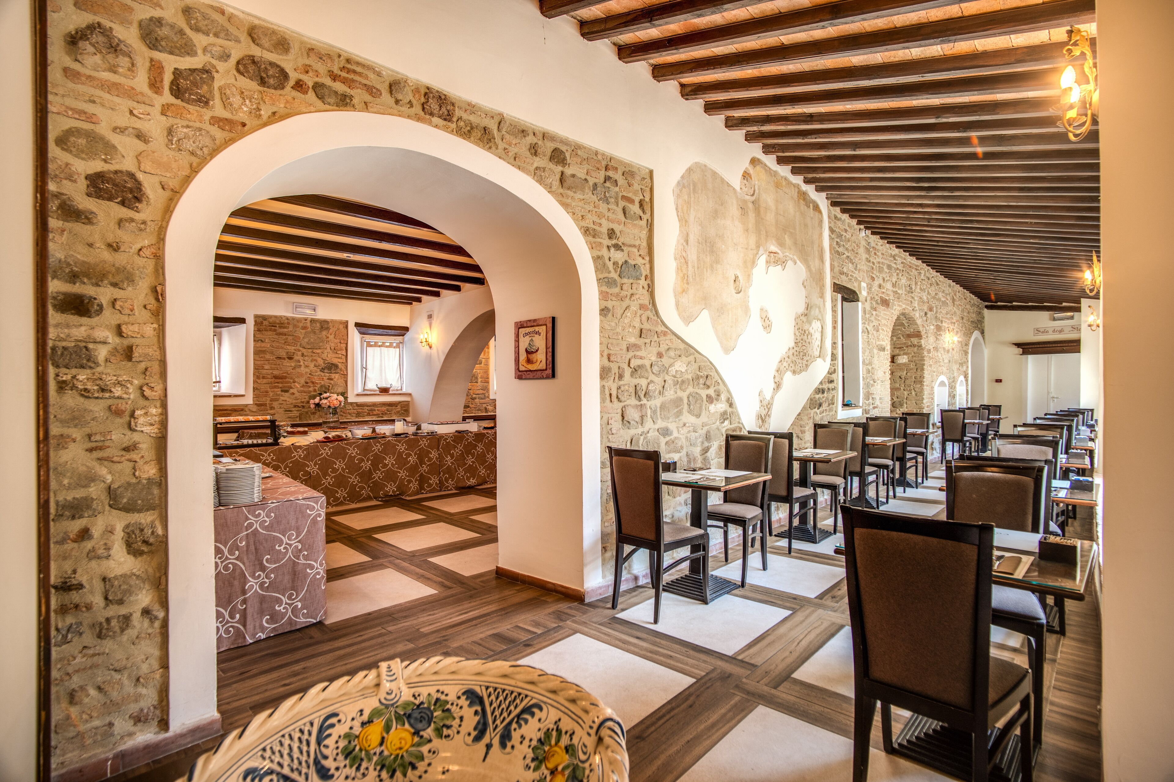 A restaurant with stone walls, wooden beams, and a checkered floor. Tables and chairs are arranged for dining.