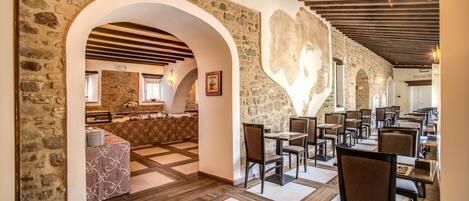 Un restaurante con paredes de piedra, vigas de madera y suelo a cuadros. Mesas y sillas dispuestas para comer.