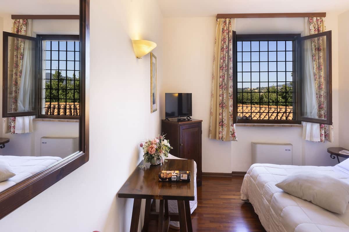 Ein Hotelzimmer mit zwei Betten, einem Schreibtisch mit Fernseher, einem Spiegel und einem fenster mit Vorhängen.
