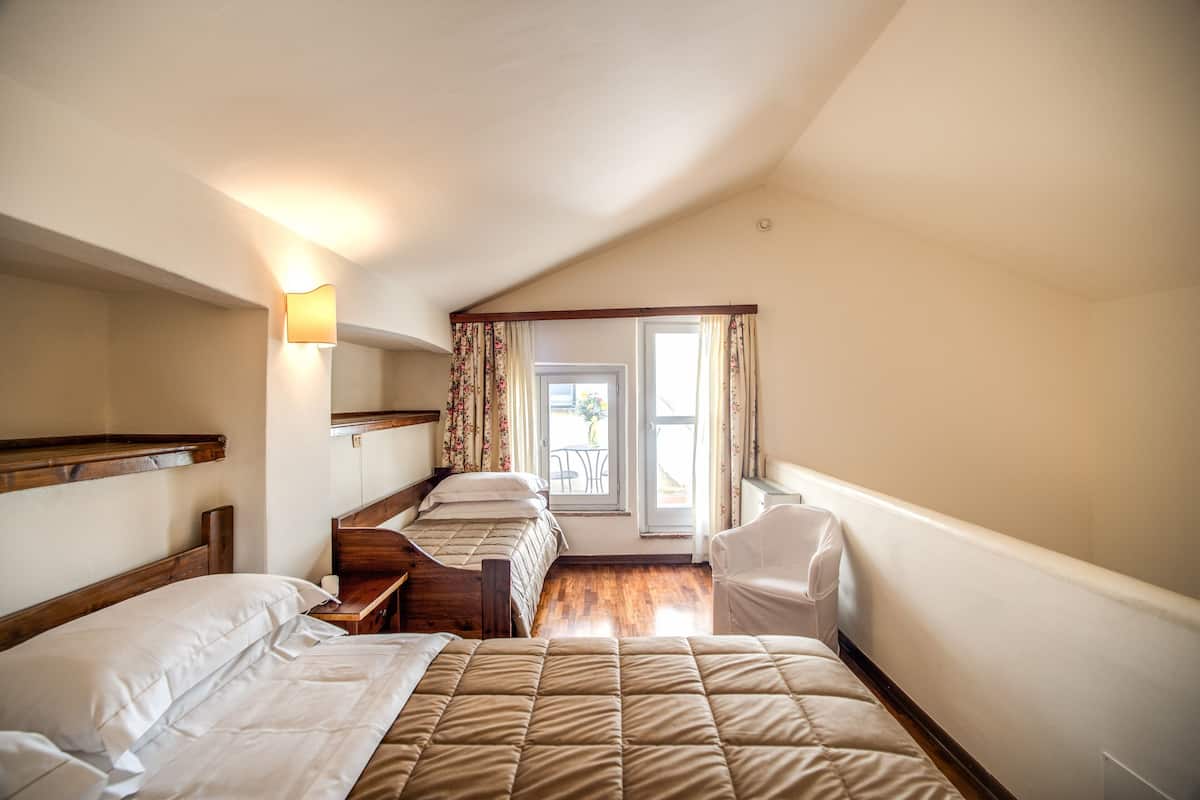 Ein Hotelzimmer mit zwei Betten, einem Schreibtisch, einem Stuhl und einem fensterbepflanzten Fenster.