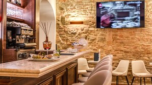 Uma área de bar com parede de pedra, televisão fixada na parede e banquetas.