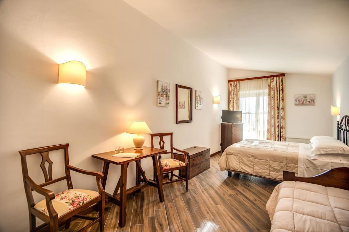 Ein Hotelzimmer mit einem Bett, einem Schreibtisch mit Lampe, zwei Stühlen, einem Fernseher und einem Fenster mit Vorhängen.
