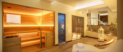A modern spa room with a sauna, a massage table, and a stone wall.