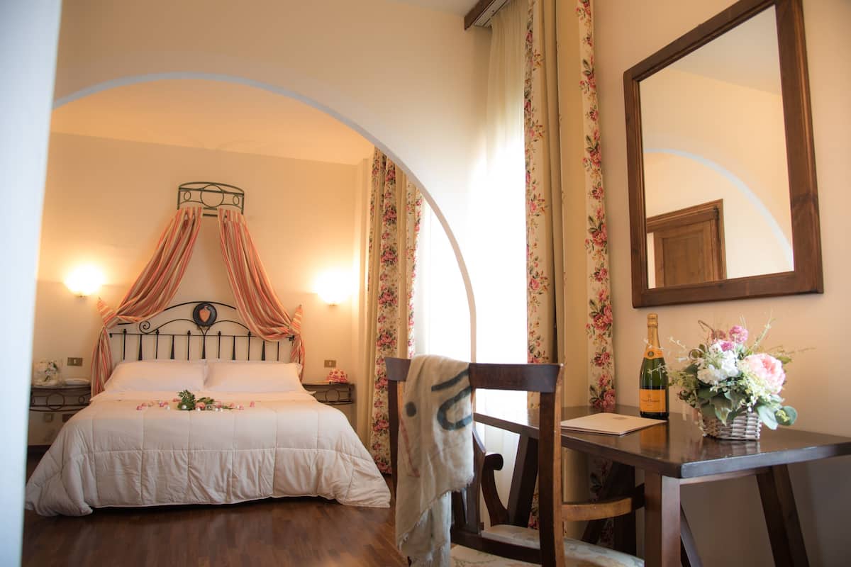 Ein Schlafzimmer mit Bett, Stuhl, Tisch, Spiegel und einer Champagnerflasche.