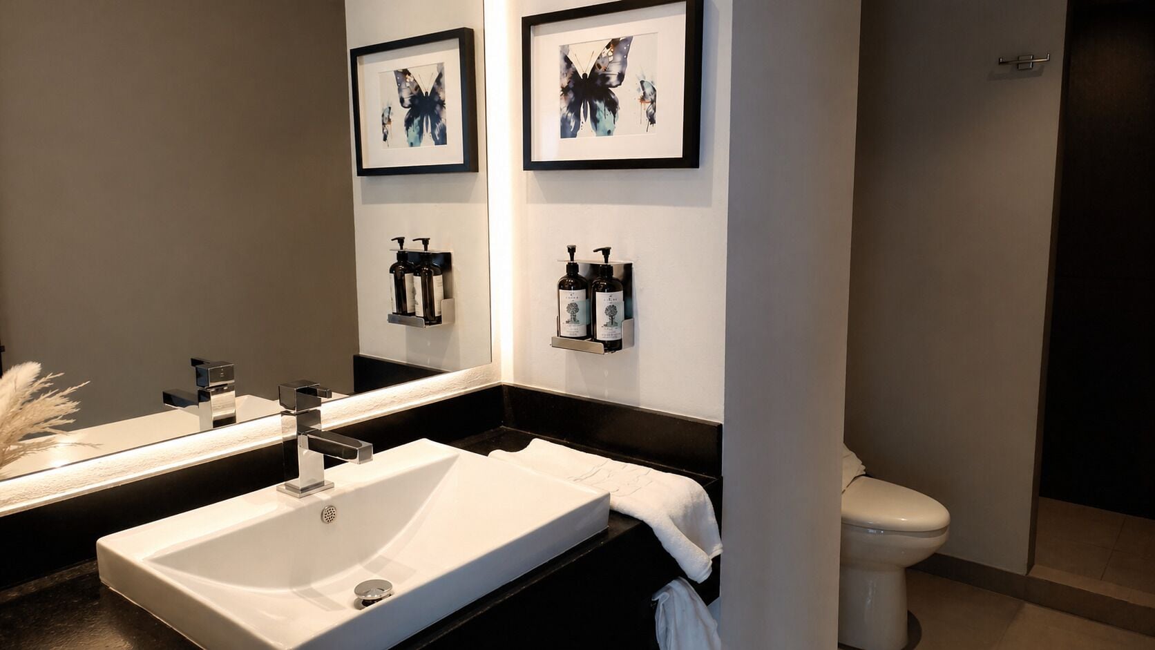 A modern bathroom with a double sink, a toilet, and framed artwork on the wall.