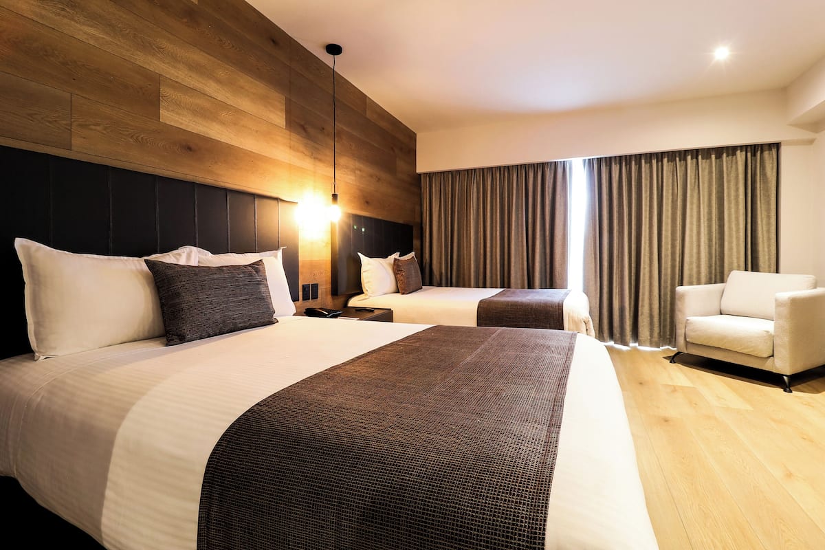 A hotel room with two beds, a sofa, a desk, and a large window with curtains.