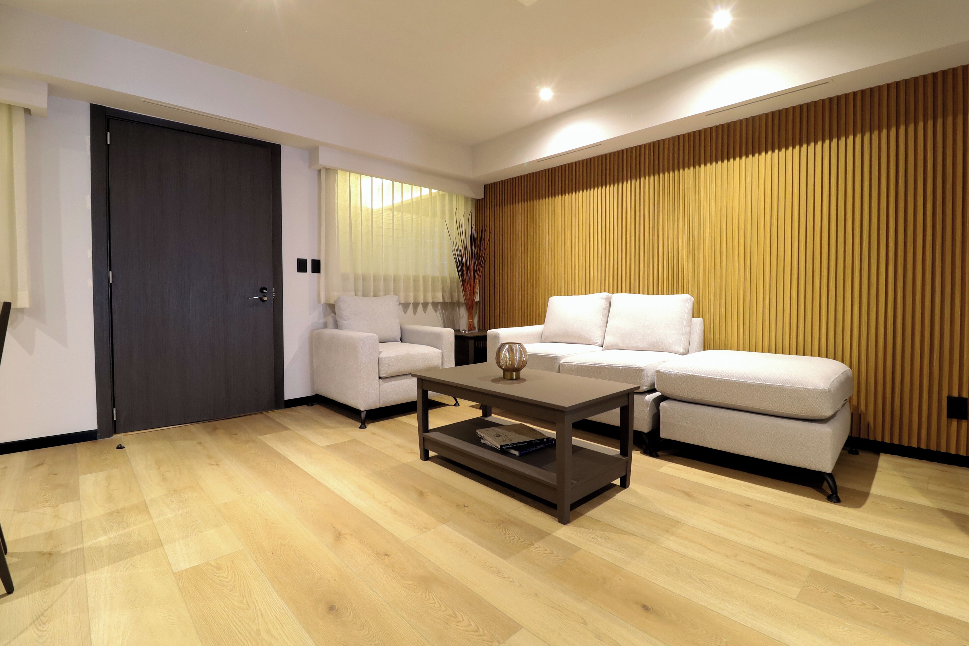 A modern living room with a dark wooden floor, a white sofa, a coffee table, and a wooden panel wall.