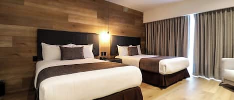 A hotel room with two beds, wooden paneling on the walls, a modern light fixture, and a view of the outdoors through large windows.