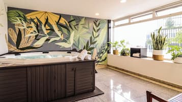 Un área de spa con una bañera de hidromasaje, un mural de hojas tropicales y plantas en macetas.