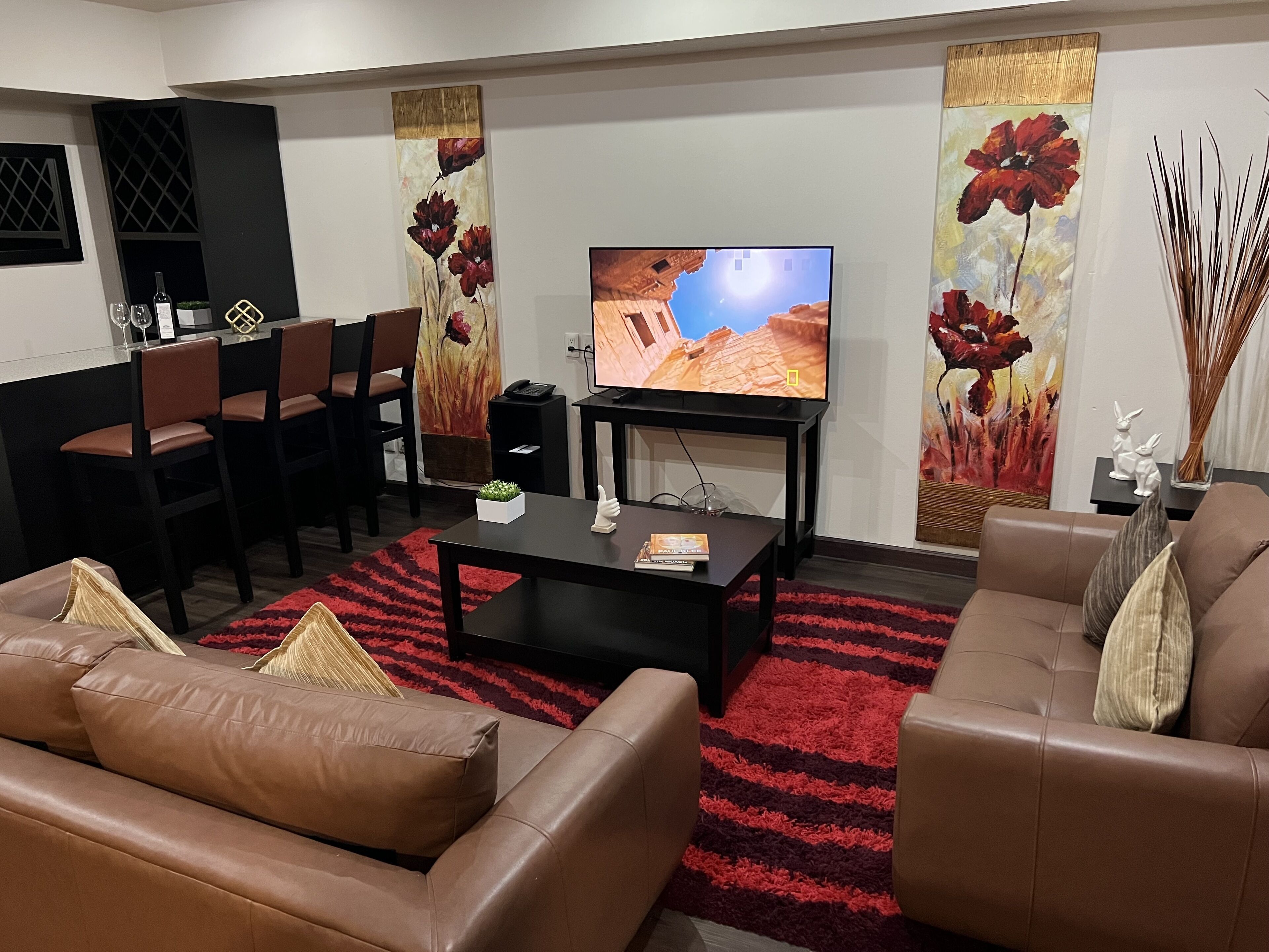 Un salon moderne avec un téléviseur, des canapés en cuir, une table basse et des tableaux décoratifs.
