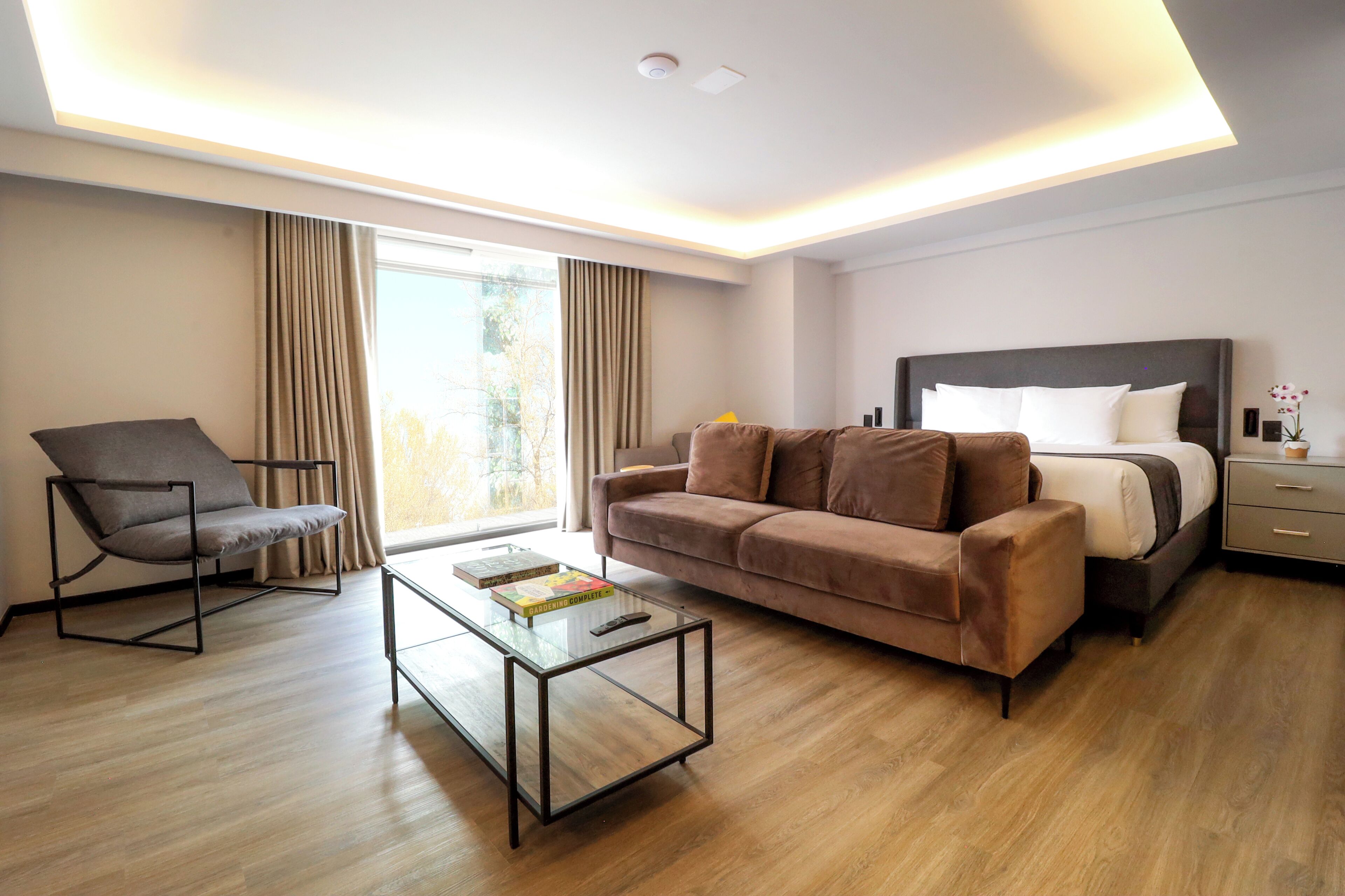 Ein modernes Hotelzimmer mit Sofa, Ohrensessel und Bett mit Nachttisch.