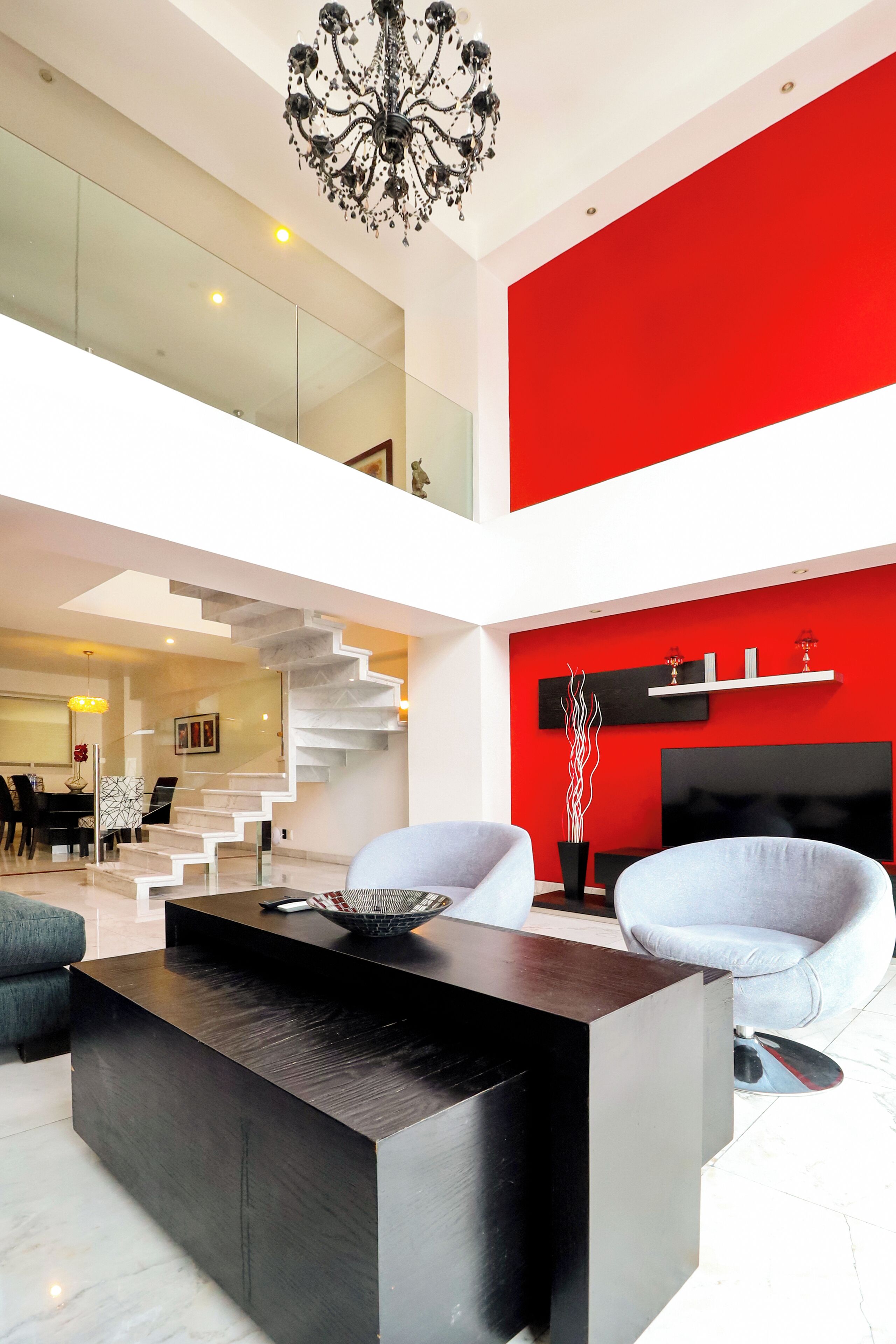 Ein modernes Wohnzimmer mit einem schwarzen Couchtisch, weißen Sofas, einer roten Akzentwand und einer Treppe, die zu einer oberen Ebene führt.