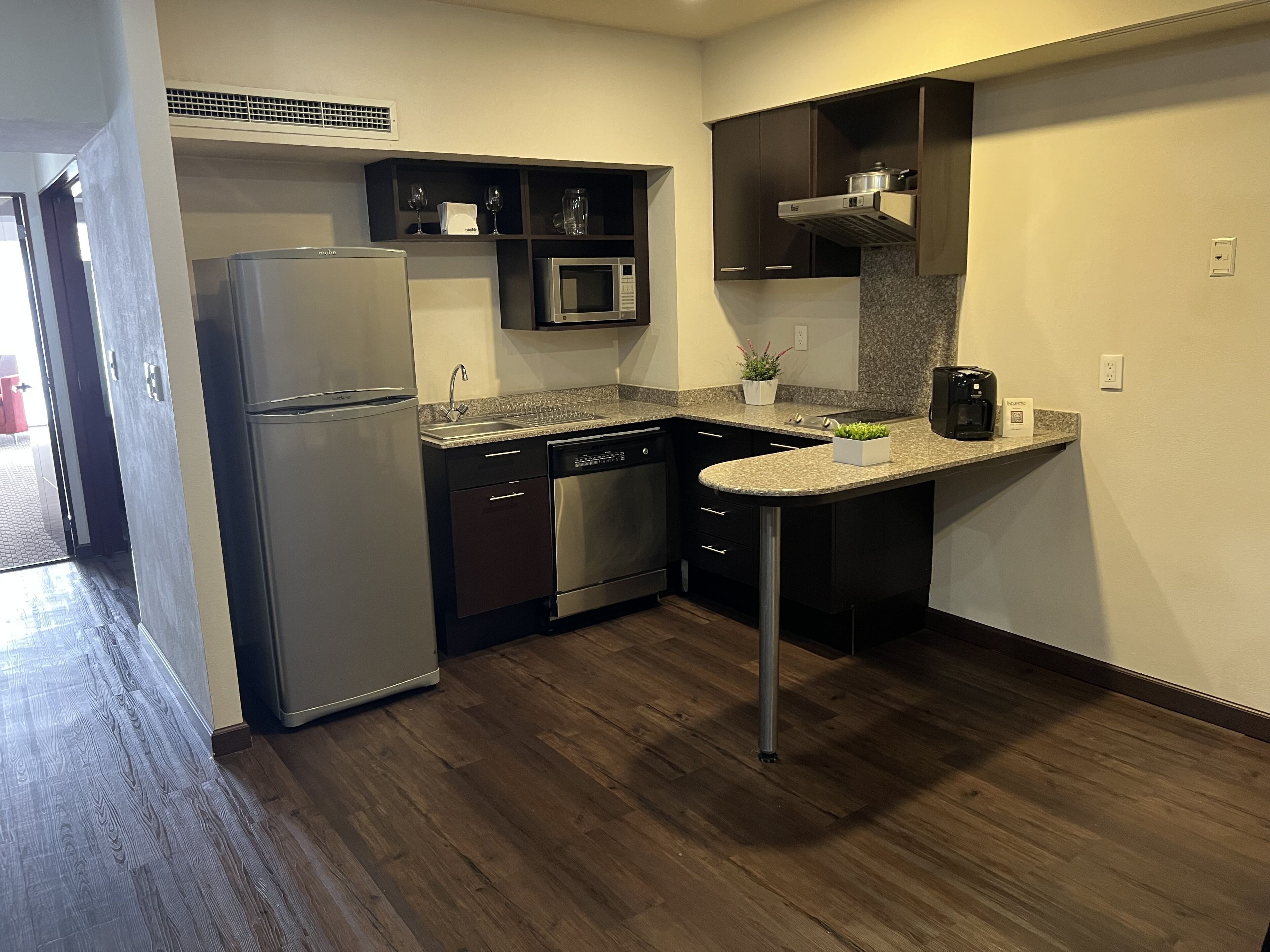 Una cocina compacta equipada con refrigerador, microondas, lavavajillas y una pequeña área de encimera con una cafetera y una planta en maceta.