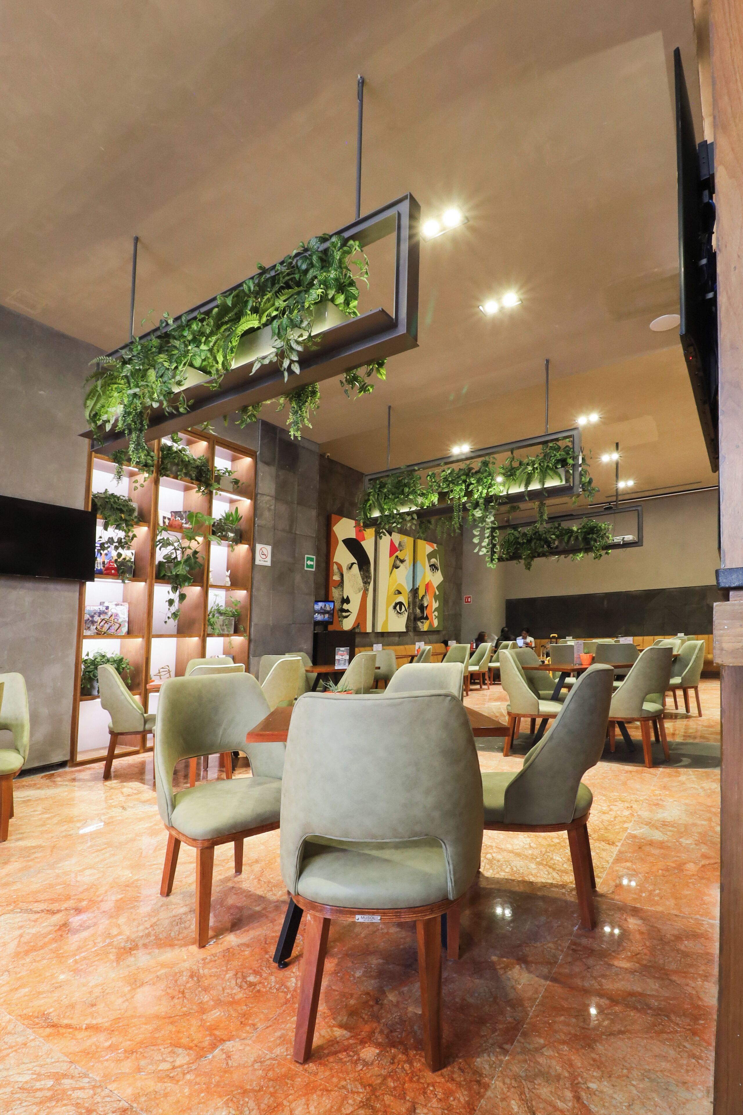 A spacious lobby with green upholstered chairs, a tiled floor, and a wall-mounted plant display.