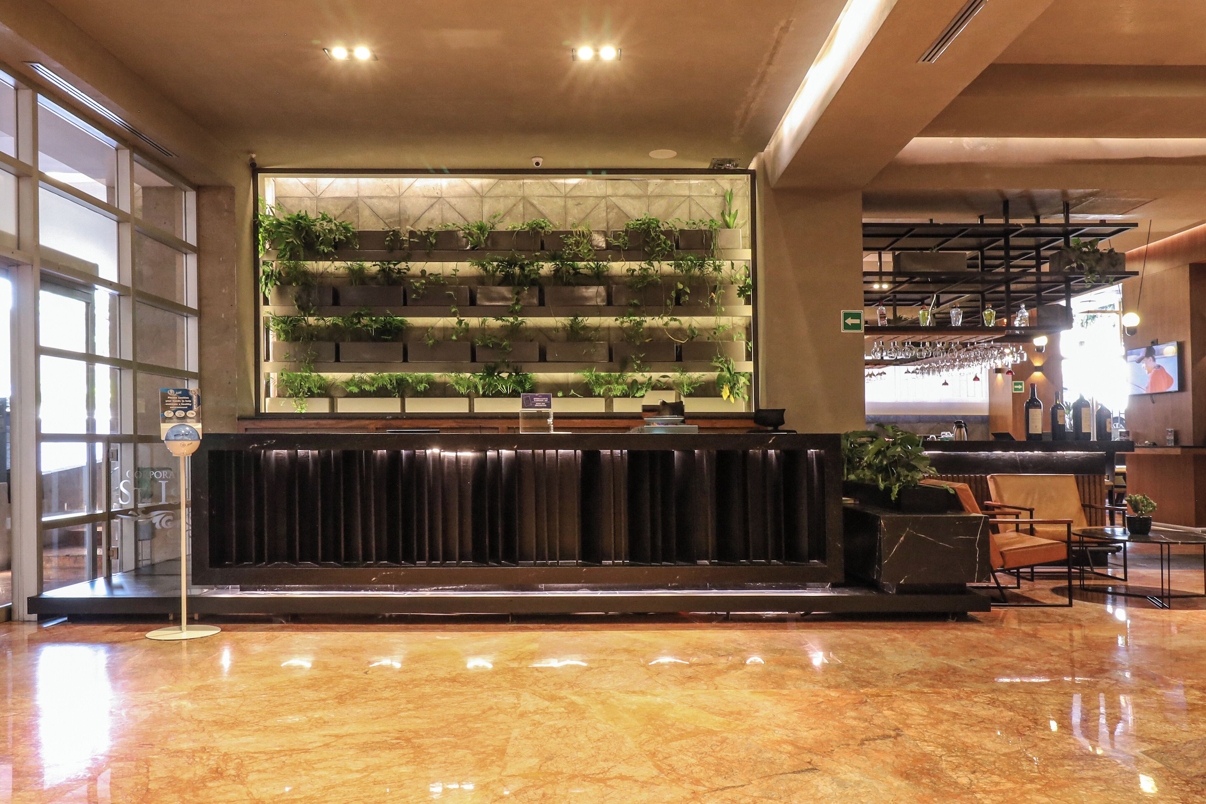 A lobby with a marble floor, a reception desk with a plant wall, and a bar area with glasses and bottles.