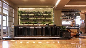 A lobby with a marble floor, a reception desk with a plant wall, and a bar area with glasses and bottles.