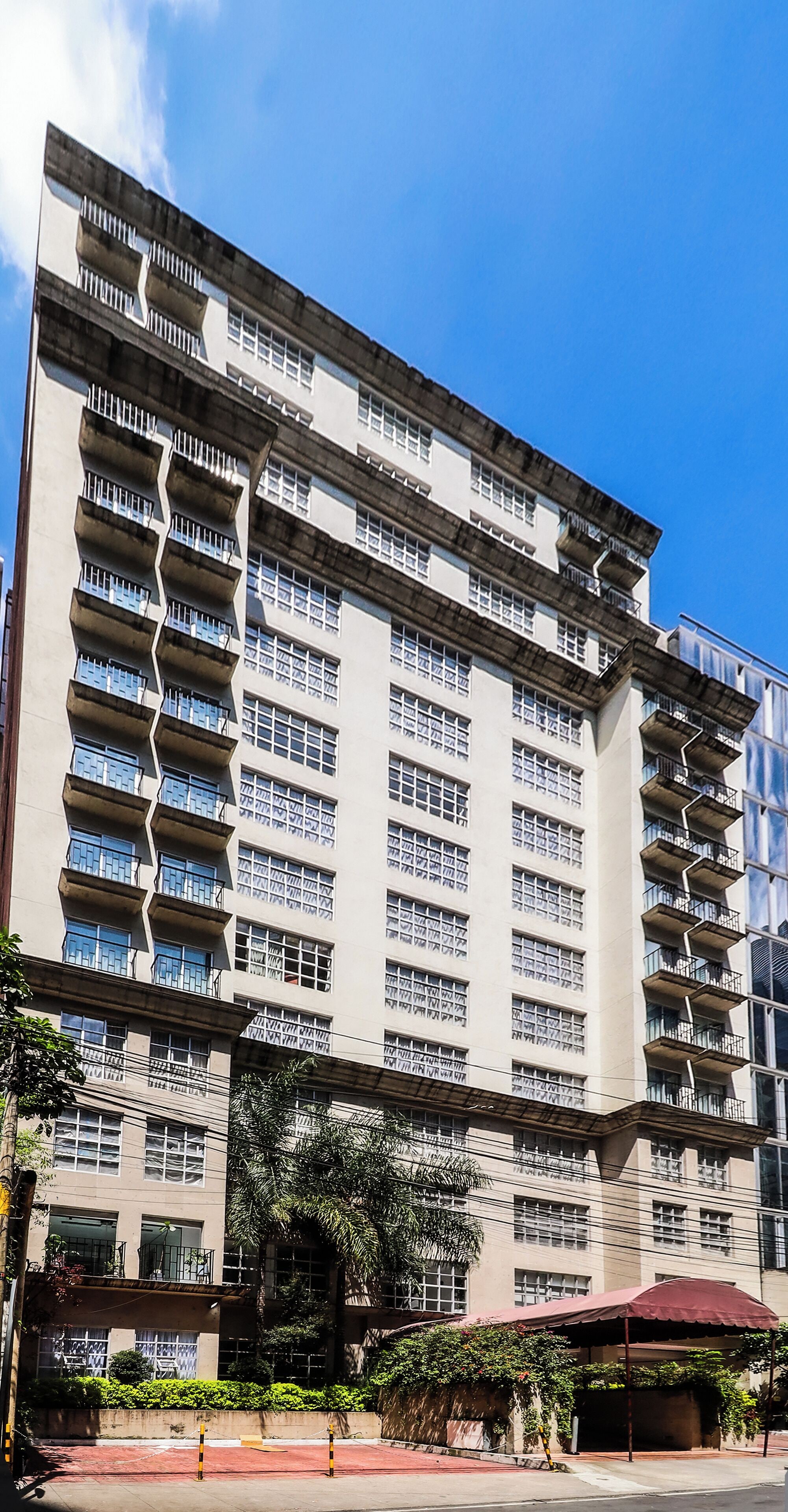 Un edificio de varios pisos con balcones, ventanas amplias y un toldo rojo.