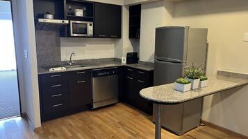 Una cocina moderna con armarios oscuros, un refrigerador de acero inoxidable, un microondas y un lavavajillas. Hay dos pequeñas macetas con plantas sobre la encimera.