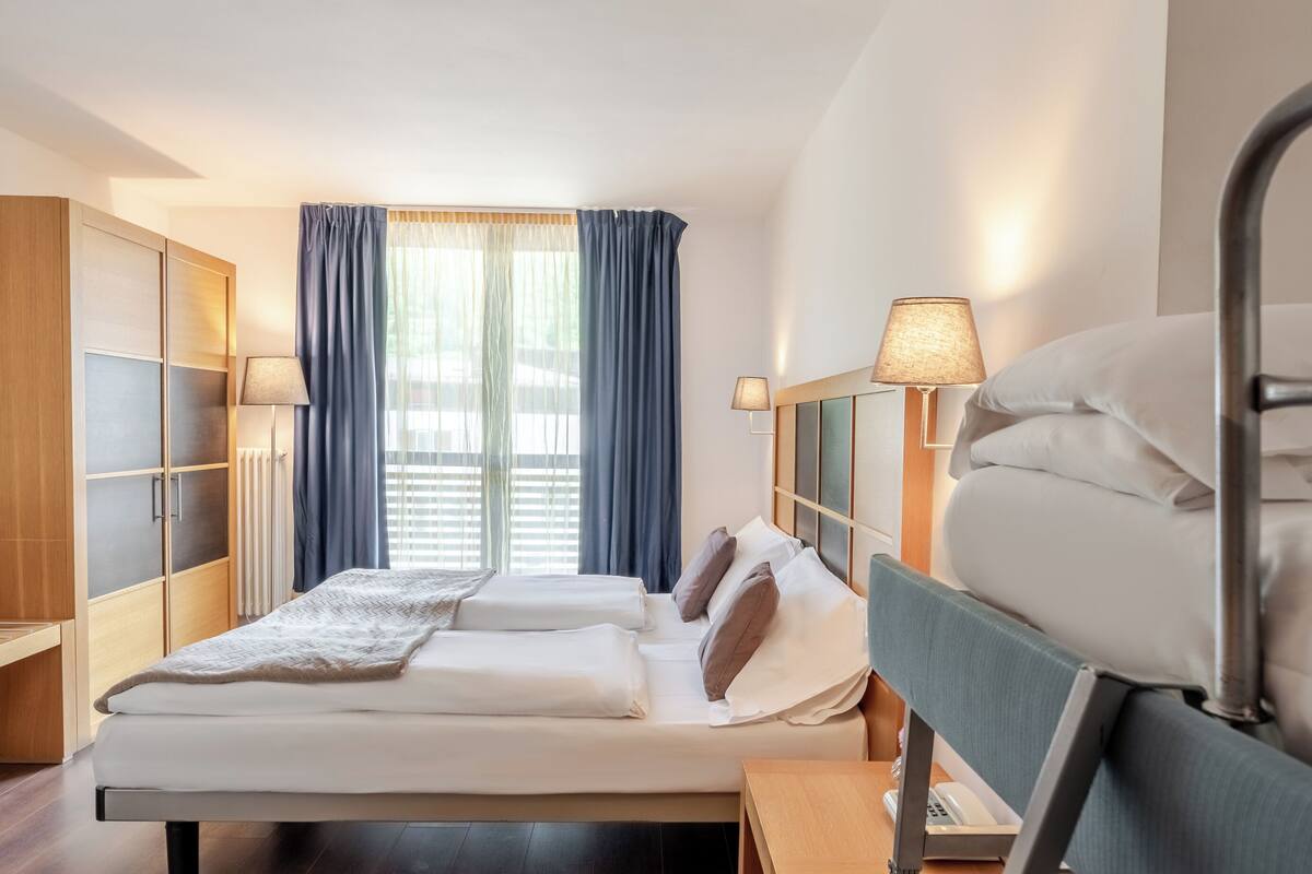 Een hotelkamer met een bed, nachtlampjes, een kledingkast en een raam met gordijnen.