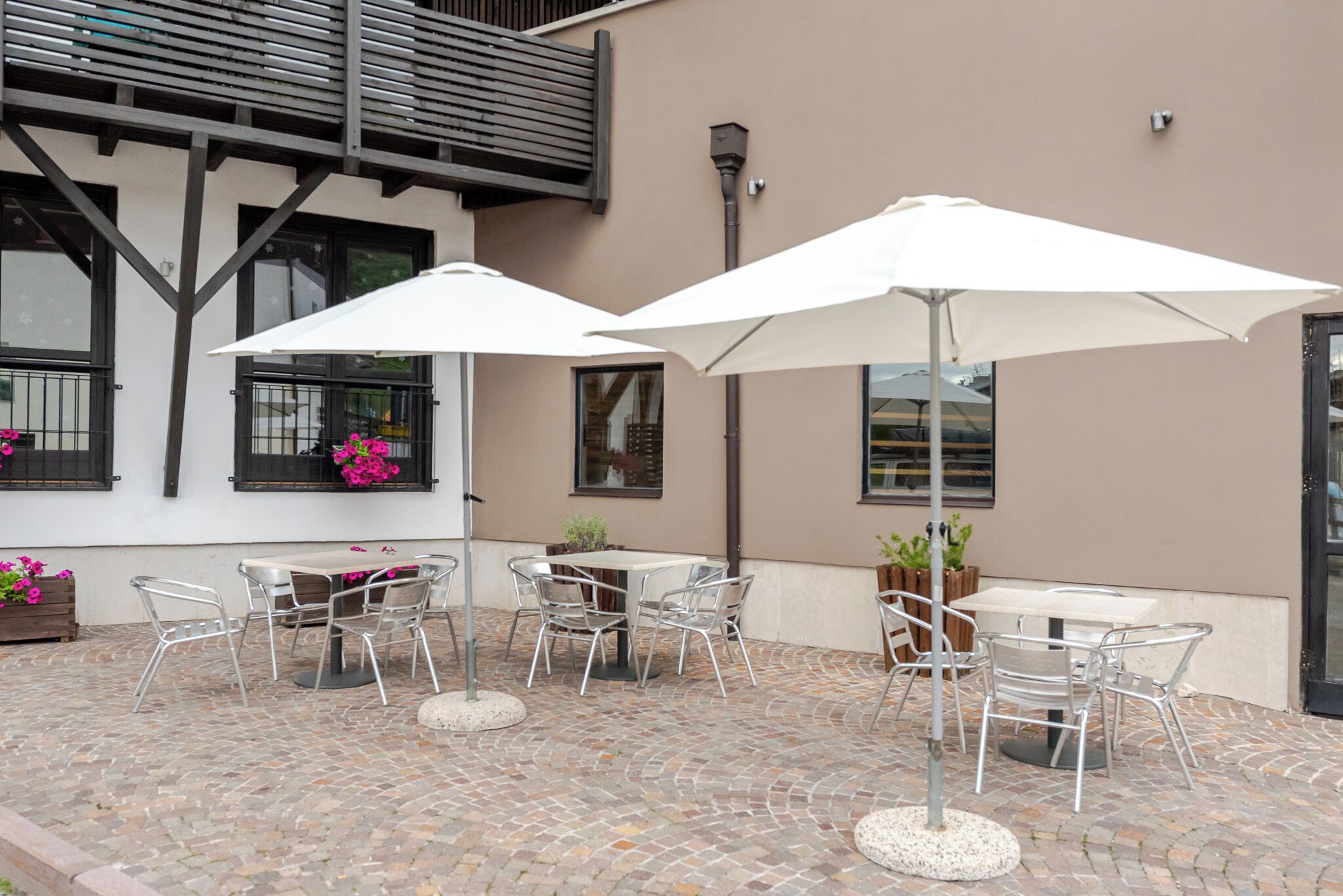 An outdoor patio with metal tables and chairs, white umbrellas, and potted plants.
