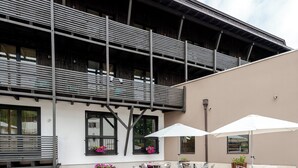 Uma área externa com mesas, cadeiras, um banco de madeira e um edifício com varanda.