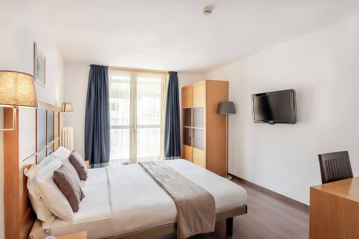 Een hotelkamer met een bed, een televisie, een bureau en een kledingkast.