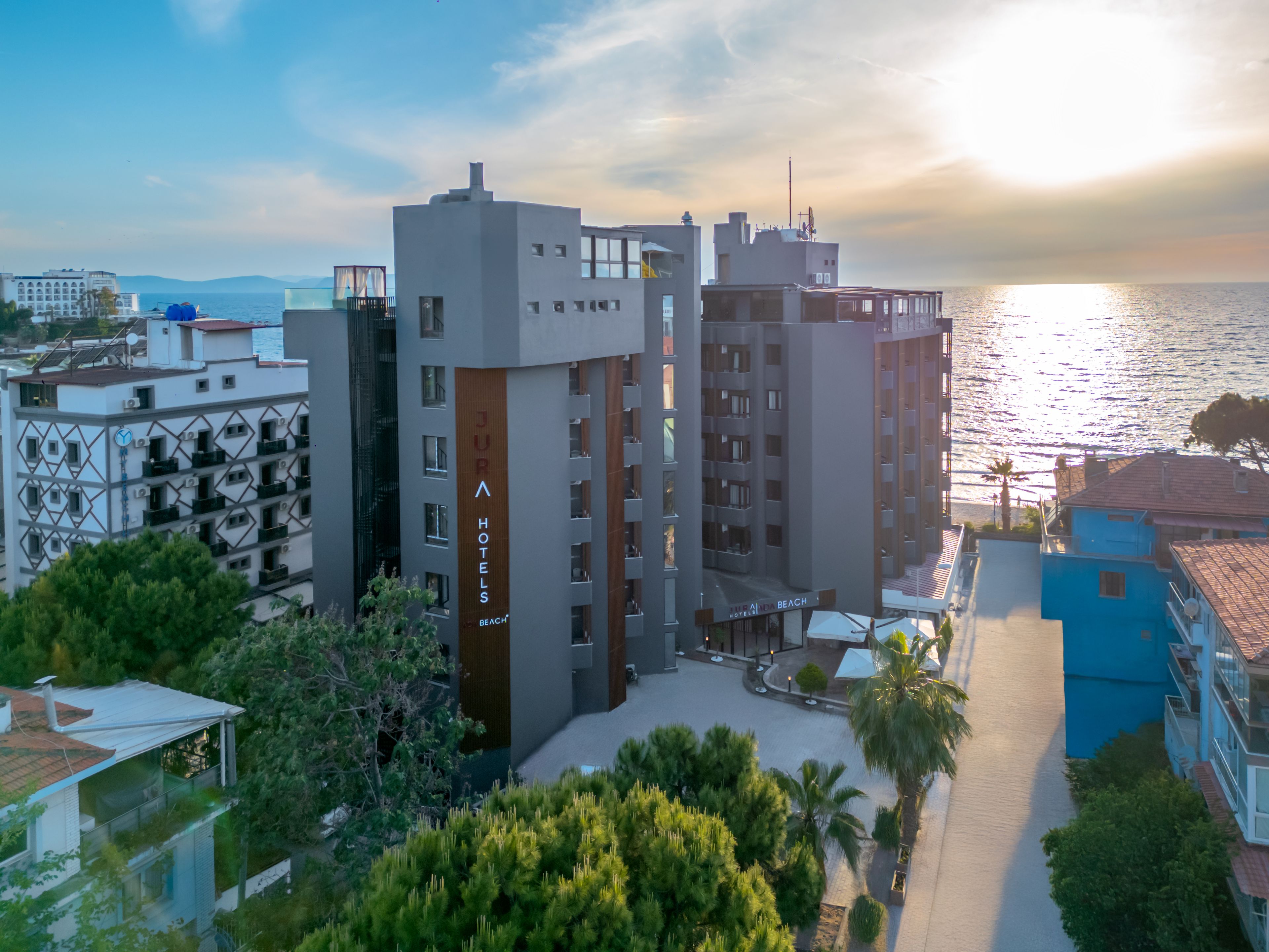 Un hotel moderno con varios pisos, un llamativo letrero de 'JURA HOTELS' y vista al mar.