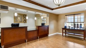A reception area with a wooden reception desk, a large mirror, pendant lighting, and a window with a view. - Comfort Inn & Suites Cordele (Cordele)