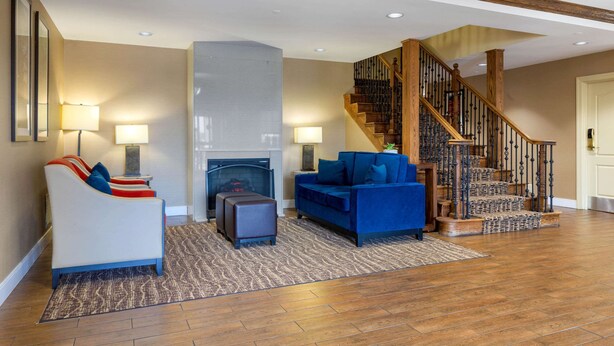 A living room with a fireplace, a blue sofa, a white sofa, and a staircase. - Comfort Inn & Suites Cordele (Cordele)