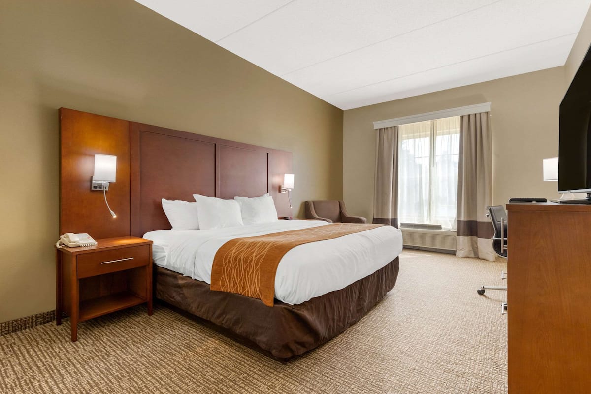 Ein Hotelzimmer mit einem großen Bett, Nachttischen, einem Schreibtisch und einem Fernseher.