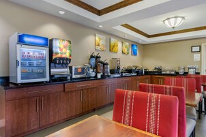 Zona de desayuno de hotel con refrigerador, cafetera y asientos.