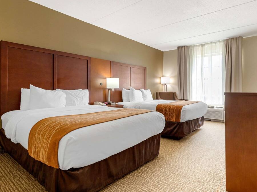 A hotel room with two beds, a wooden headboard, a desk, and a television.