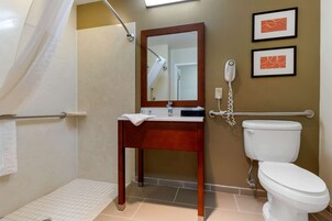 A bathroom with a wooden vanity, a white toilet, a shower with a glass door, and a telephone mounted on the wall.