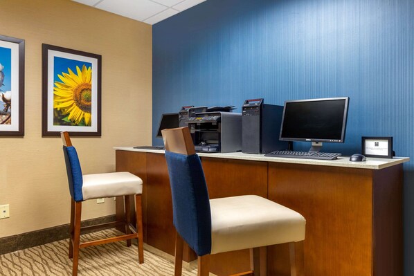 A hotel reception desk with two chairs, a computer, a printer, and framed pictures on the wall.