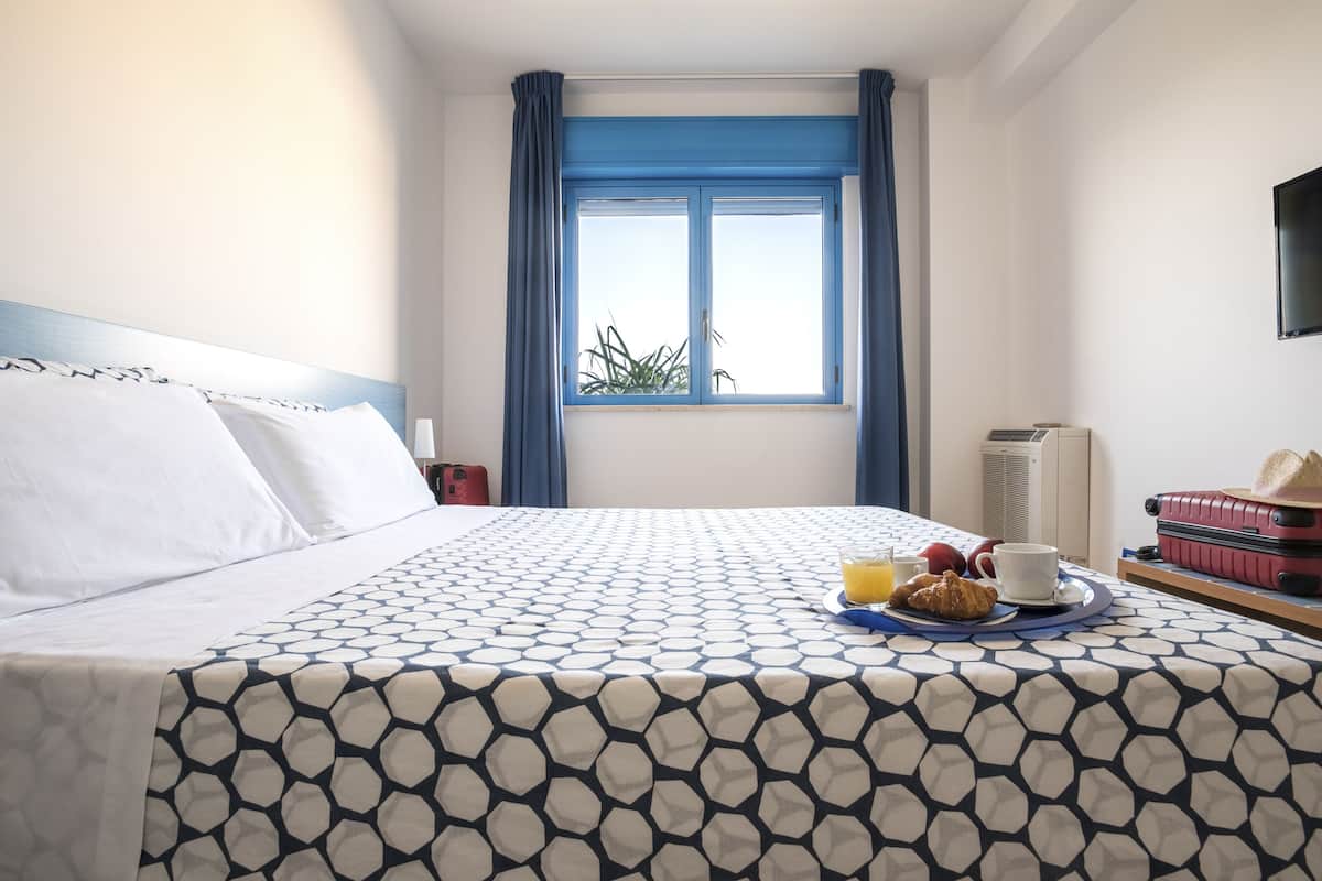 Habitación de hotel con cama, bandeja de desayuno, ventana y televisor en la pared.