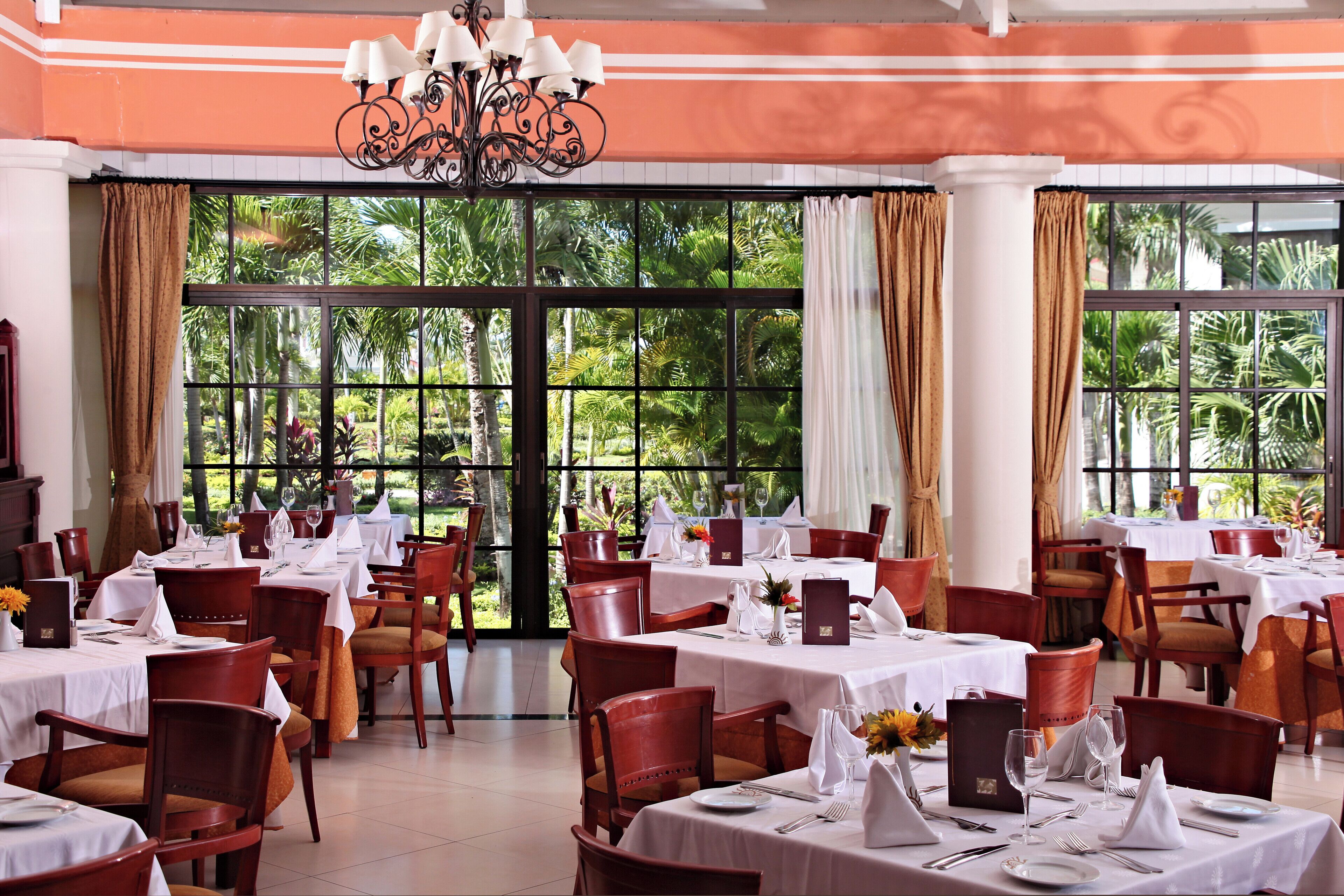 Ein Restaurant mit gedeckten Tischen, großen Fenstern mit Vorhängen und einer Kronleuchter.