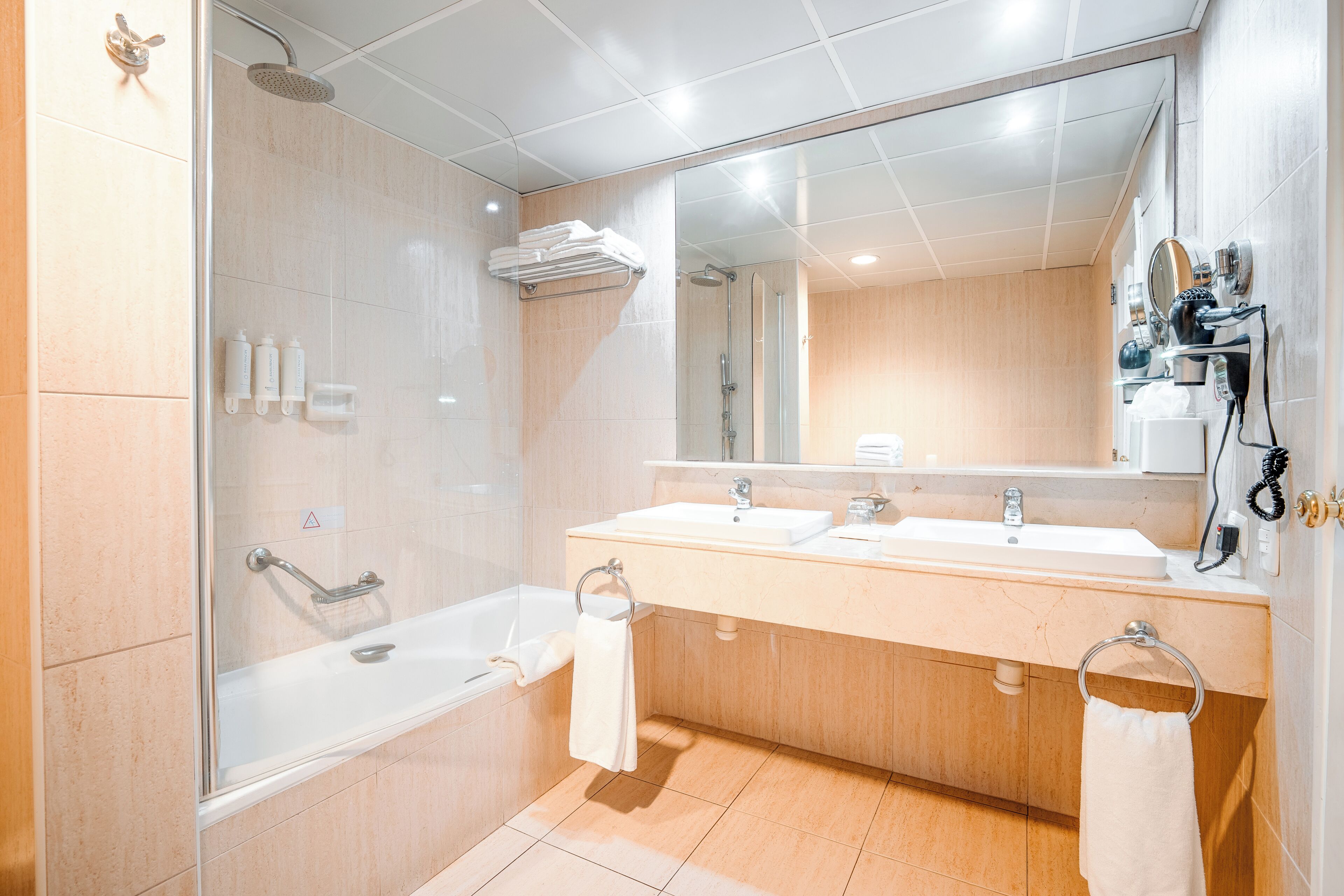 A modern bathroom with a bathtub, two sinks, a shower, and a large mirror.