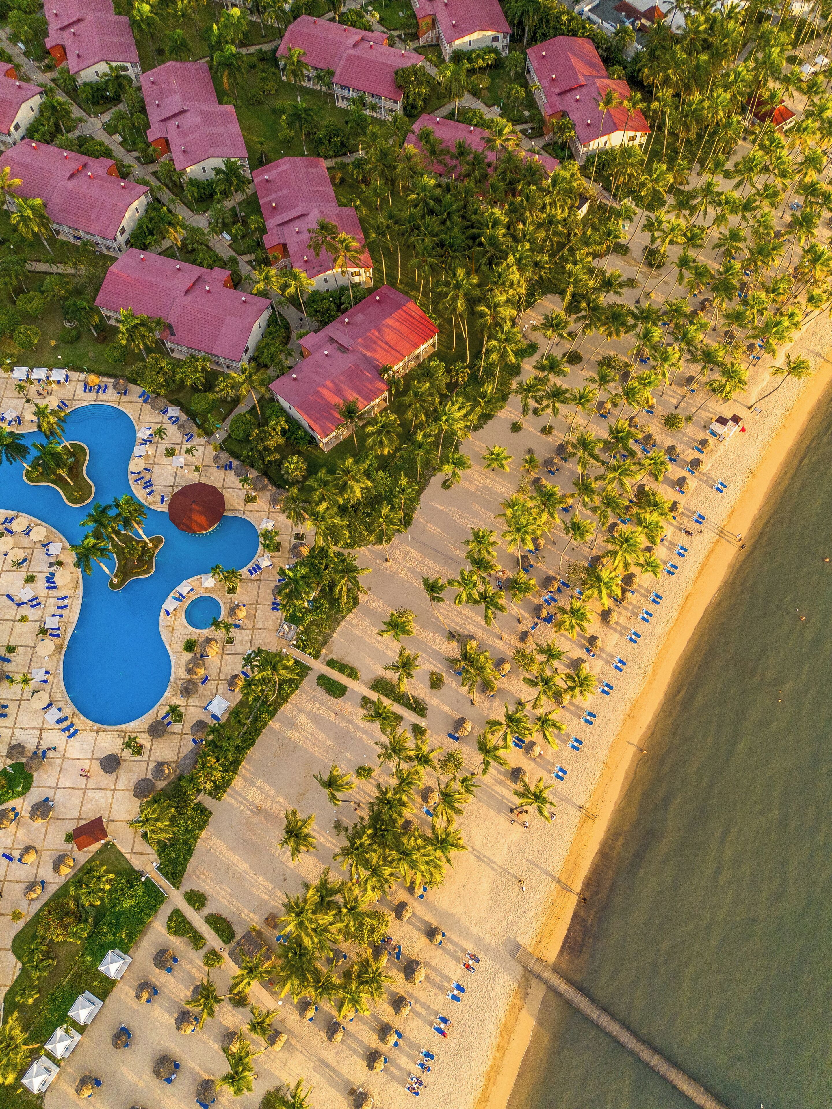 Luchtbeeld van een resort met meerdere gebouwen, een zwembad en een strandgebied met ligbedden.