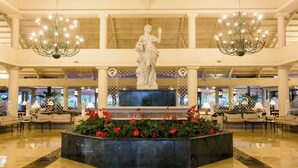 A lobby with a central statue, seating areas, and chandeliers.