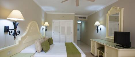 A hotel room with a bed, bedside lamps, a desk with a computer, a ceiling fan, and a large mirror.