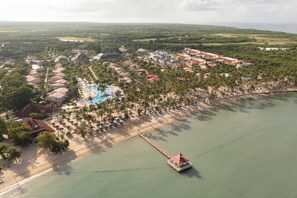 An aerial view of a resort with a swimming pool, beach, and a pier extending into the water.