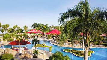 Un resort con piscina central, sillas de descanso, palmeras y edificios con techo rojo.