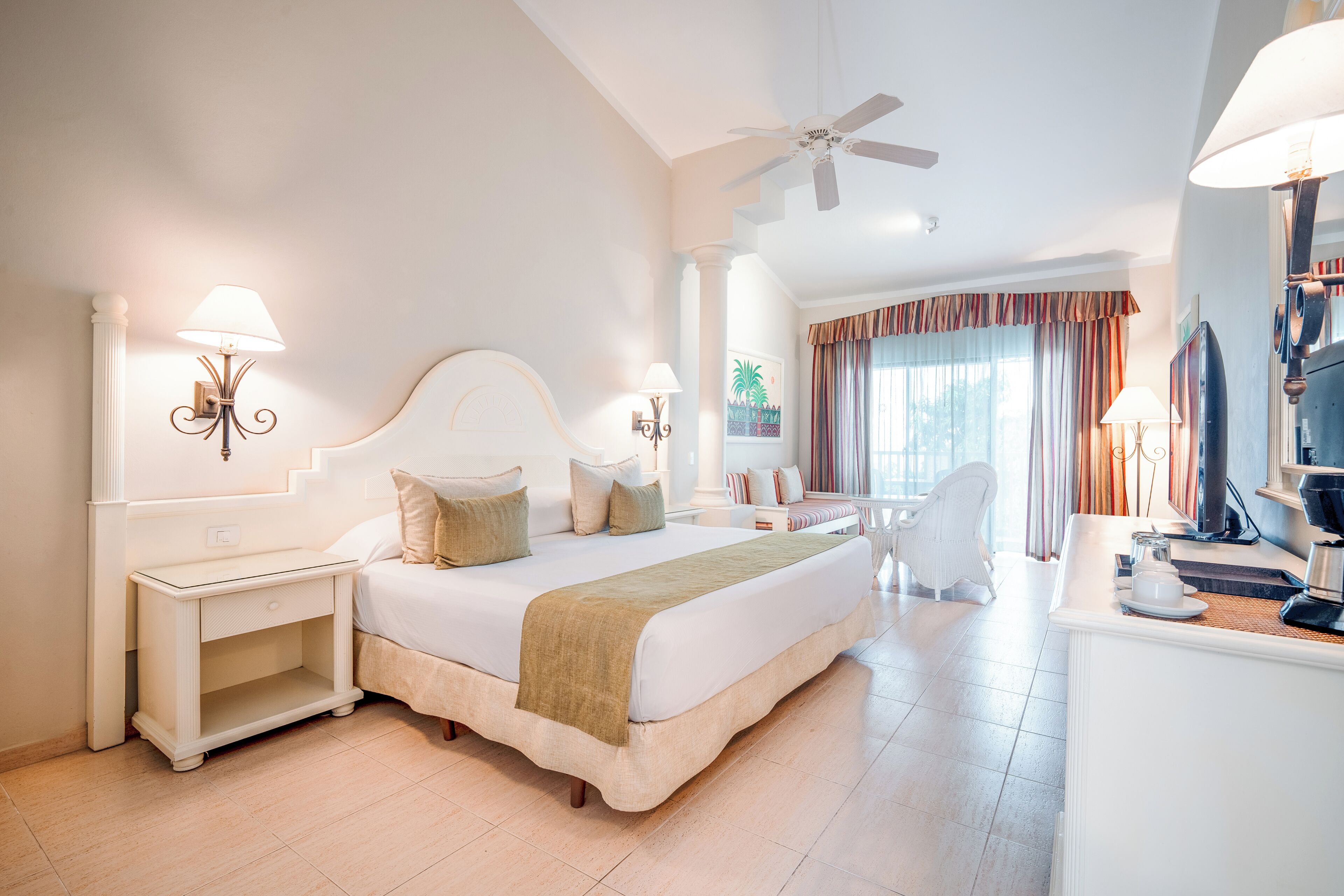A hotel room with a large bed, bedside tables, a desk, a chair, and a ceiling fan.
