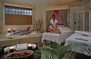 A spa room with two massage tables, a bathtub, and a shower area.