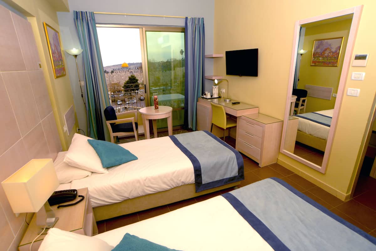 A hotel room with two beds, a desk, a chair, a TV, and a balcony with a city view.