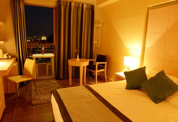 Habitación de hotel con cama, escritorio, silla, una mesita y vista panorámica de la ciudad.